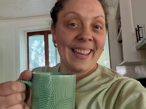 Sammy smiling with a cup of tea in a green mug
